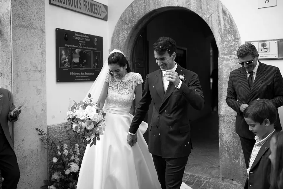 Bride and groom coming out through a stone archway among the guests