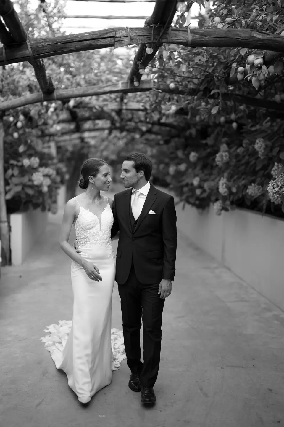 Black and white photo of the couple holding hands under the pergola.