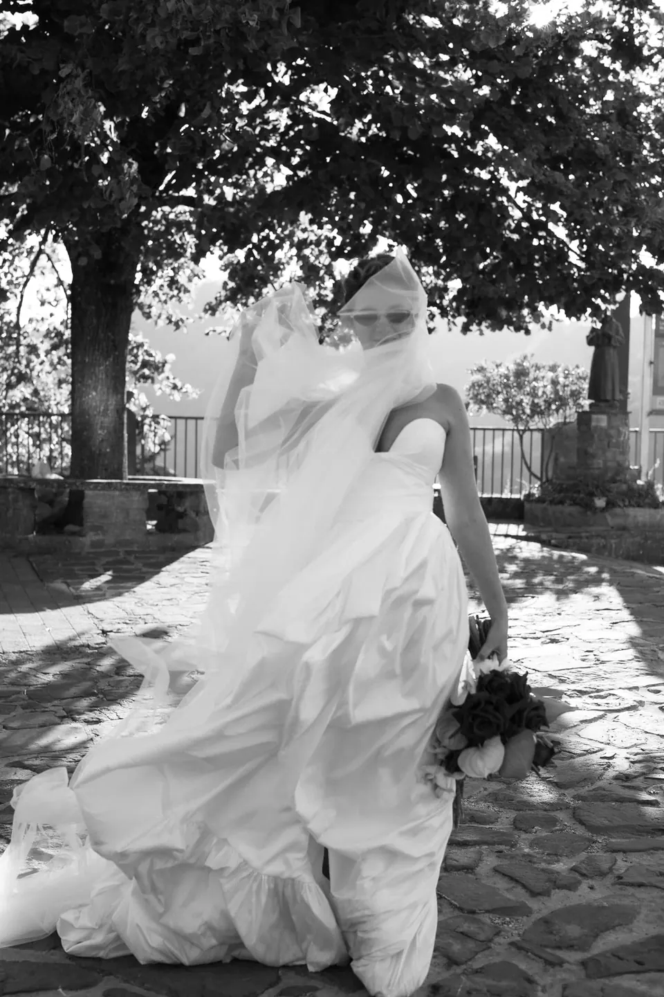 Foto in bianco e nero dell'abito e del velo della sposa mossi dal vento.