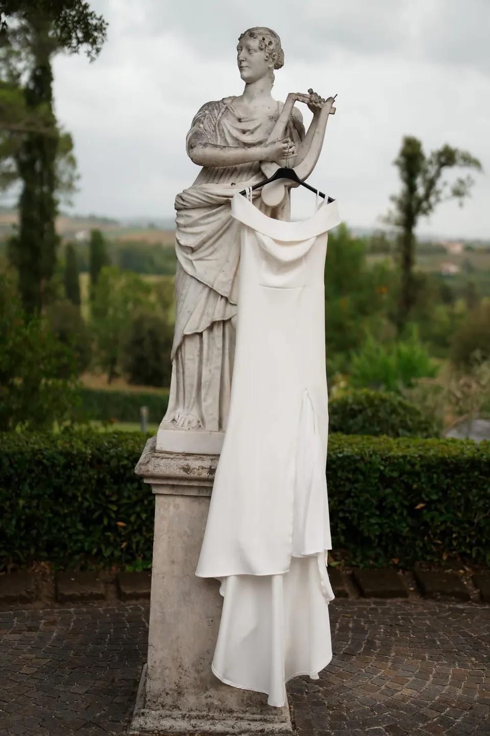 Estatua clásica de mármol en los jardines, con el vestido de novia colgado de ella.