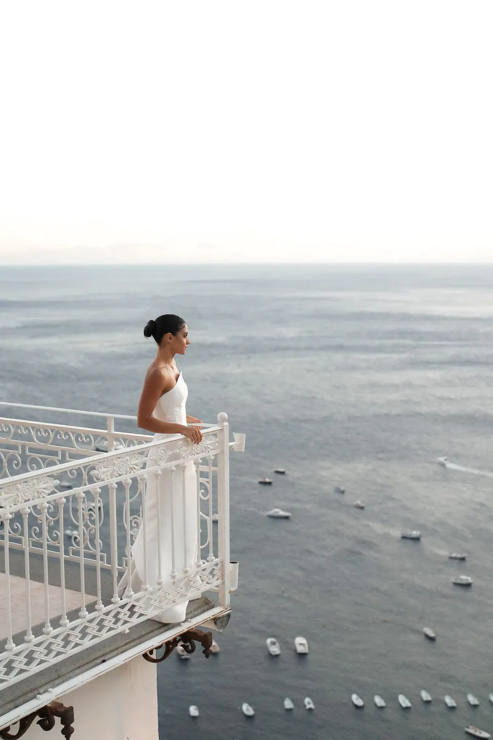 Bride standing on the edge of a terrace high above the sea and the boats.