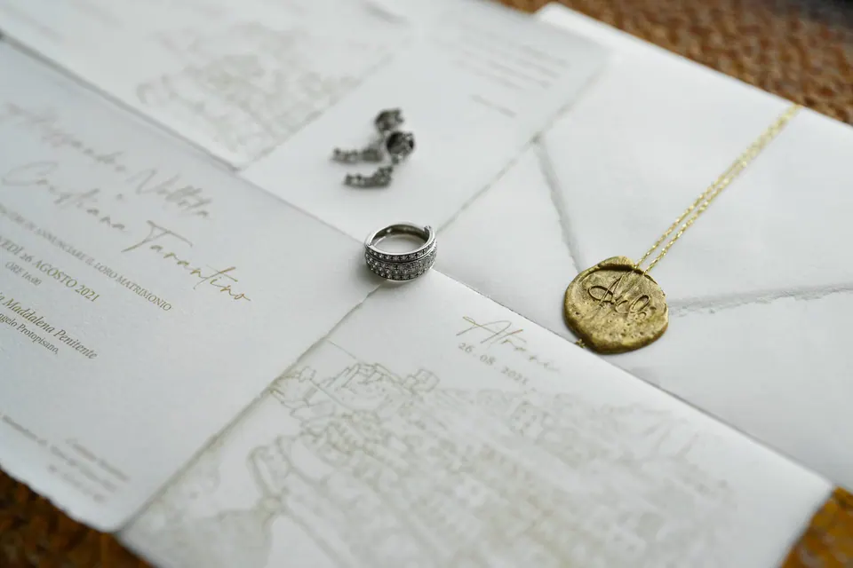 Goldkette, Einladung und Eheringe nebeneinander.