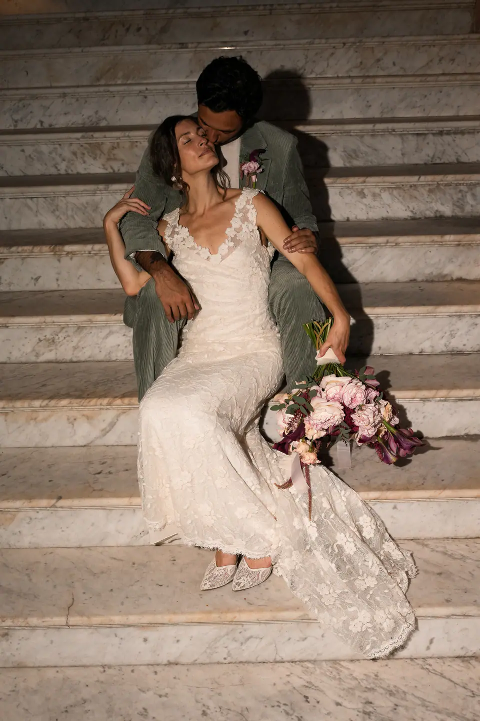 Couple kissing on old stone steps at night, her bouquet in her lap.