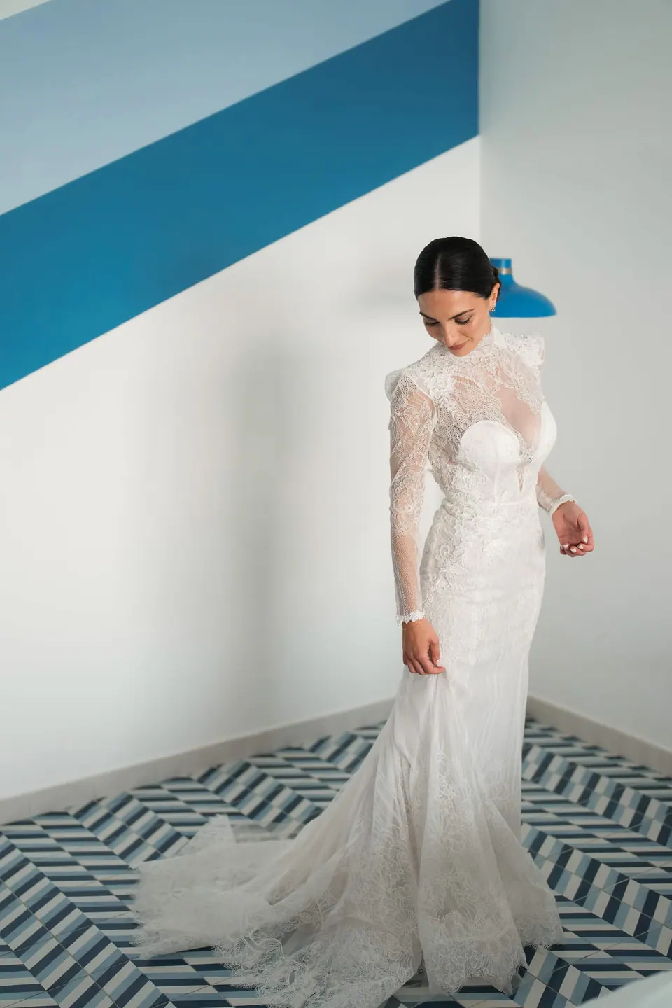 Die Braut im Spitzenkleid in einem Raum mit blauem Streifen an der Wand.