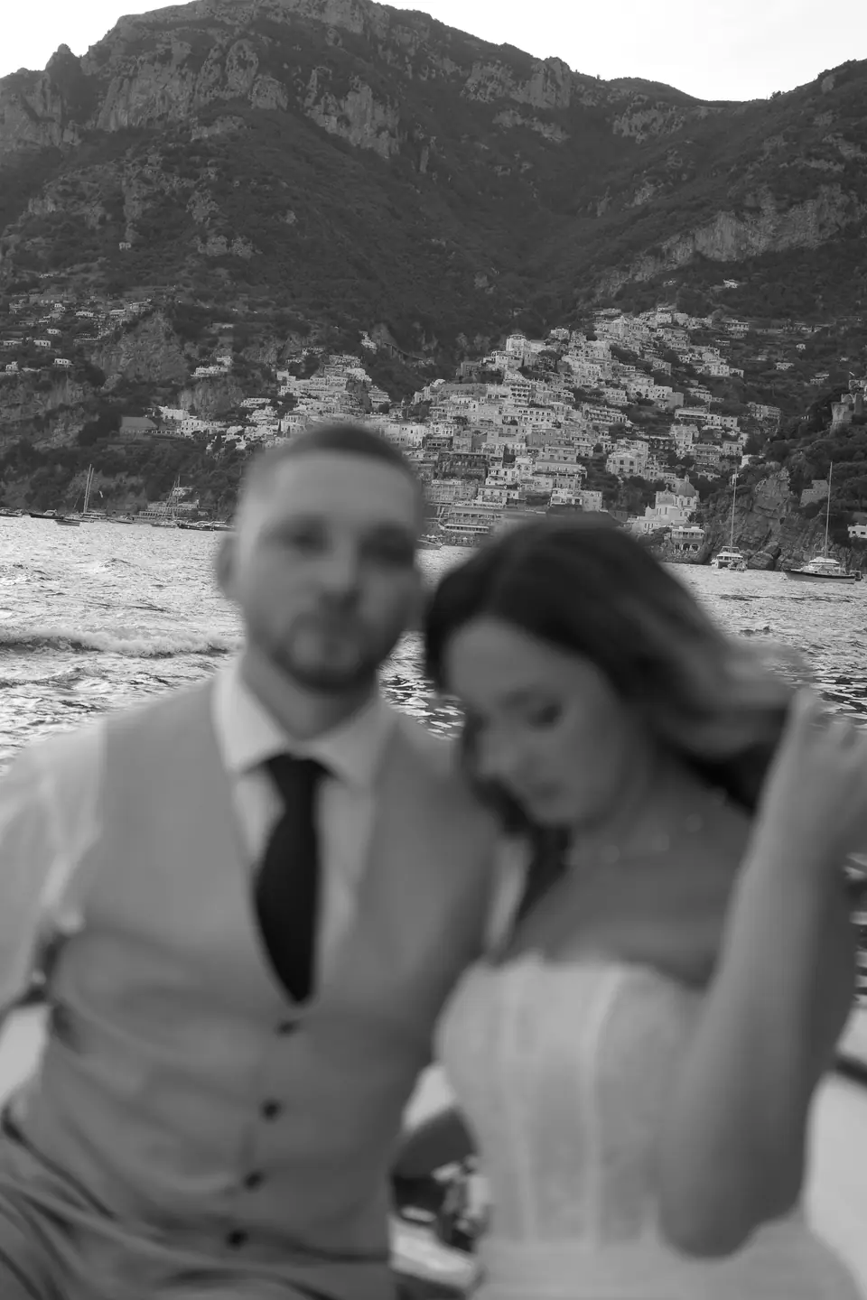 Black and white portrait of the couple on the boat, Positano behind them.