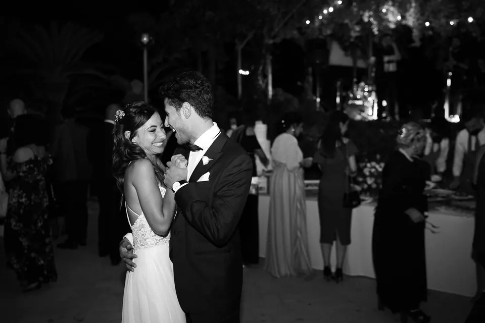 Foto in bianco e nero degli sposi che ballano tra gli invitati di sera.