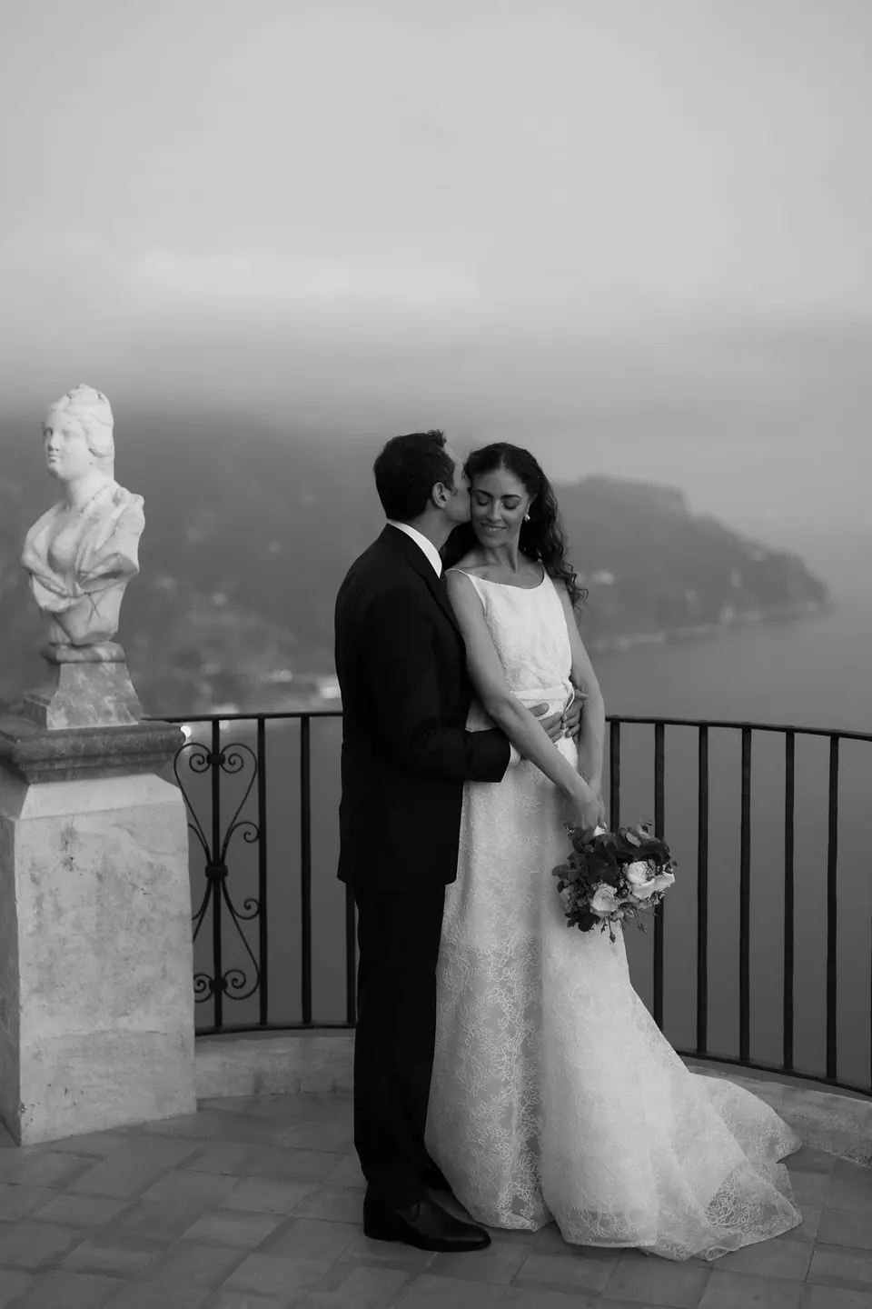 Black and white portrait of the couple on the Terrace of Infinity, a bust beside them.