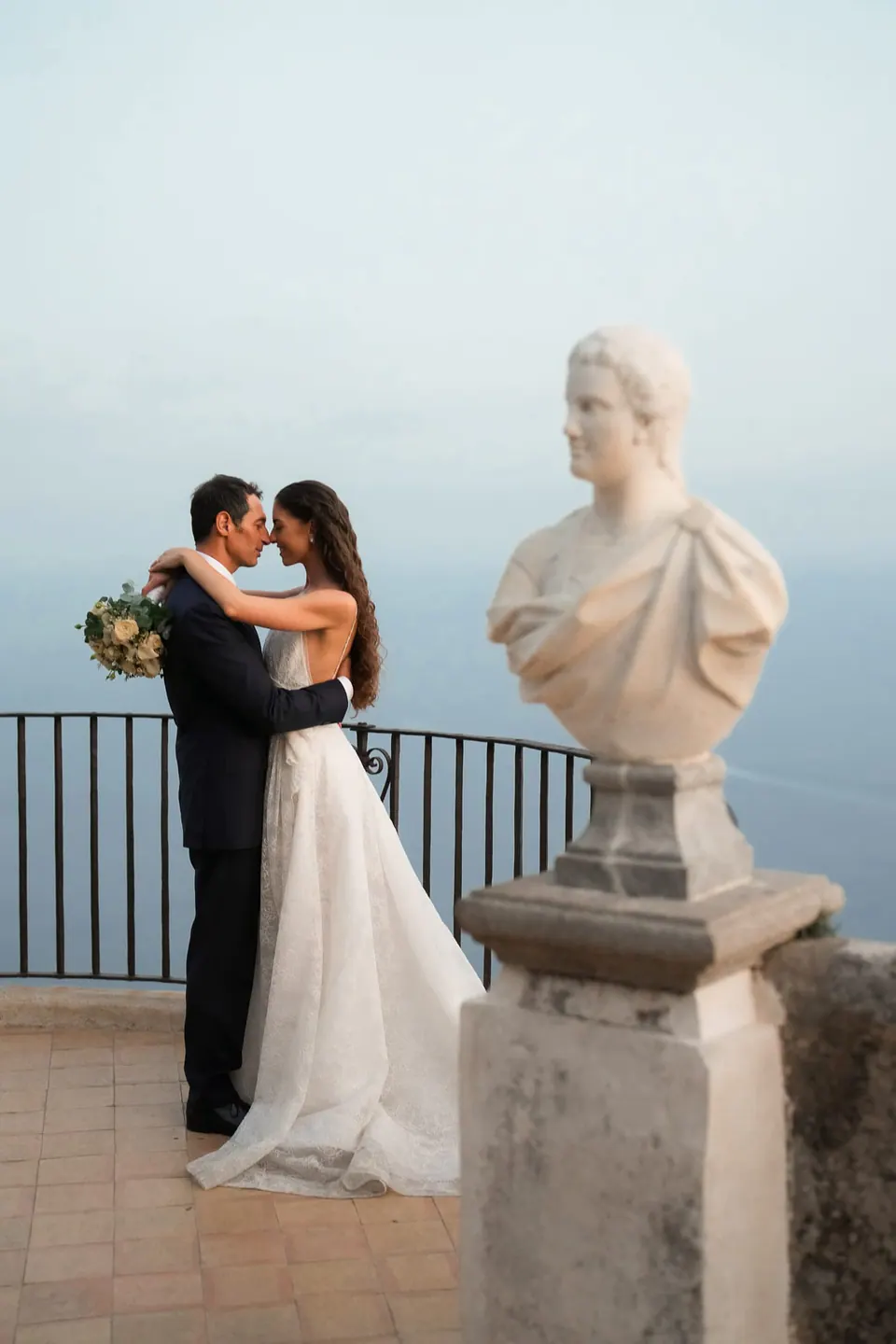 Bride and groom embracing on the Terrace of Infinity beside a marble bust.