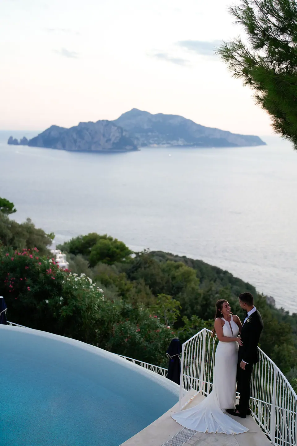 Bride and groom by the infinity pool, Capri on the horizon at dusk.