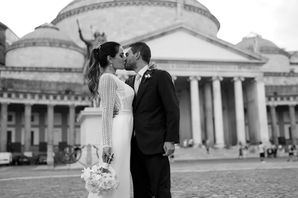 Black and white photo of the couple kissing in Piazza del Plebiscito, the basilica behind them.