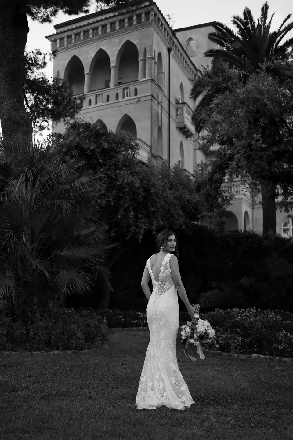 Black and white photo of the bride on the lawn in front of a historic villa.