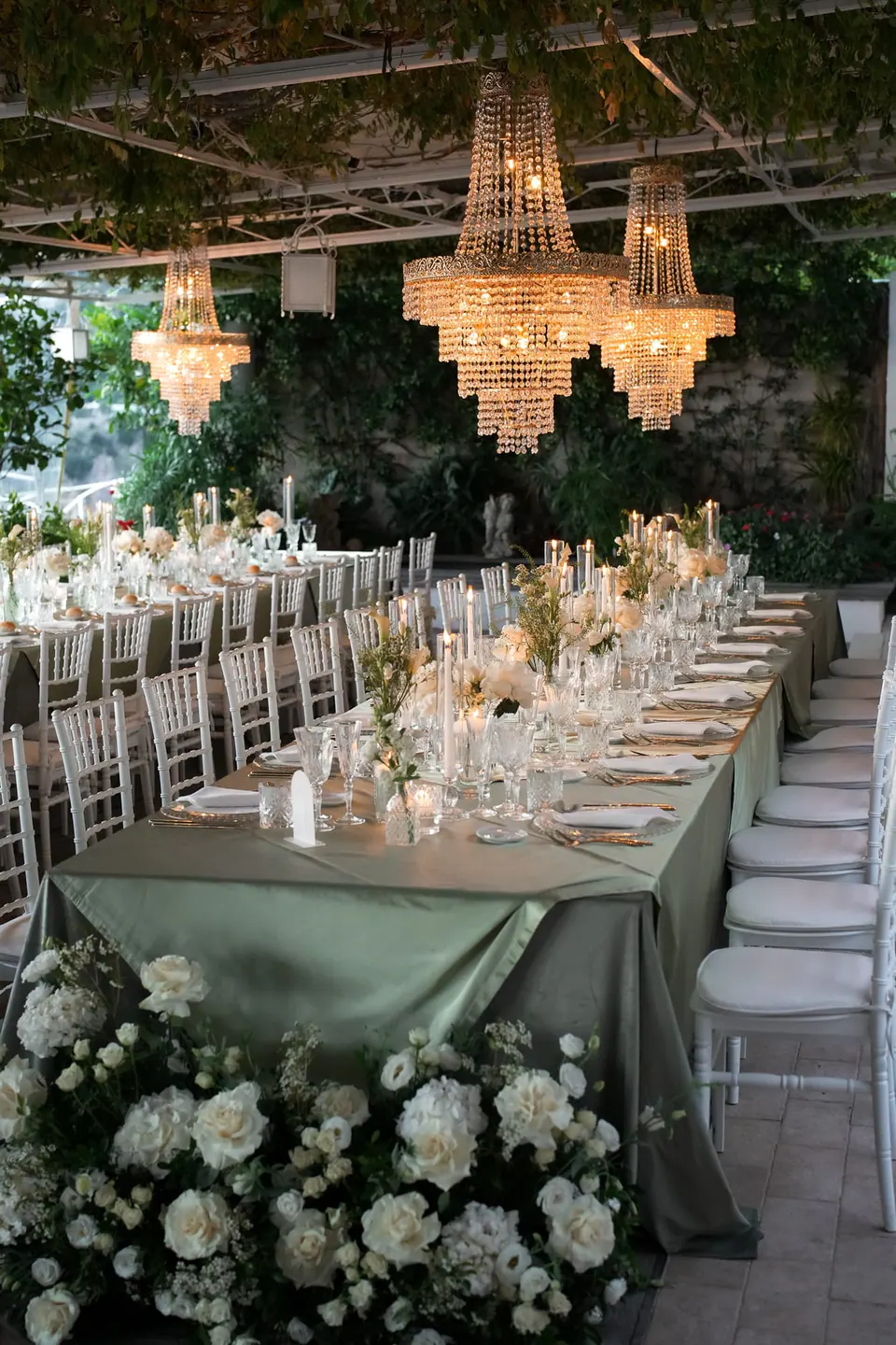 Reception table under the pergola with crystal chandeliers and white flowers.