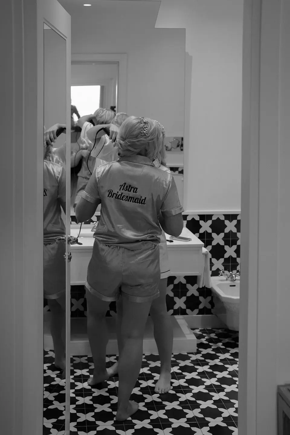 Black and white photo of a bridesmaid in a robe getting ready at the mirror