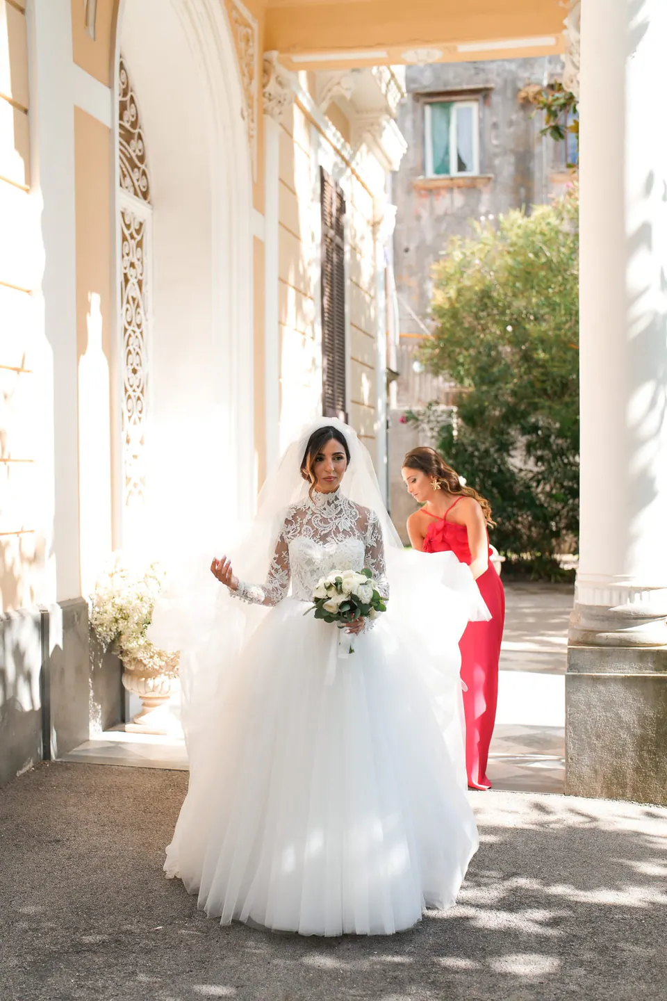 Bride walking under a portico with a guest in red