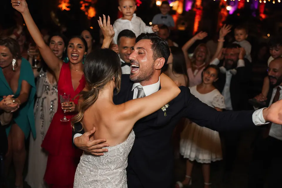 Couple laughing while dancing under string lights during the night celebration.
