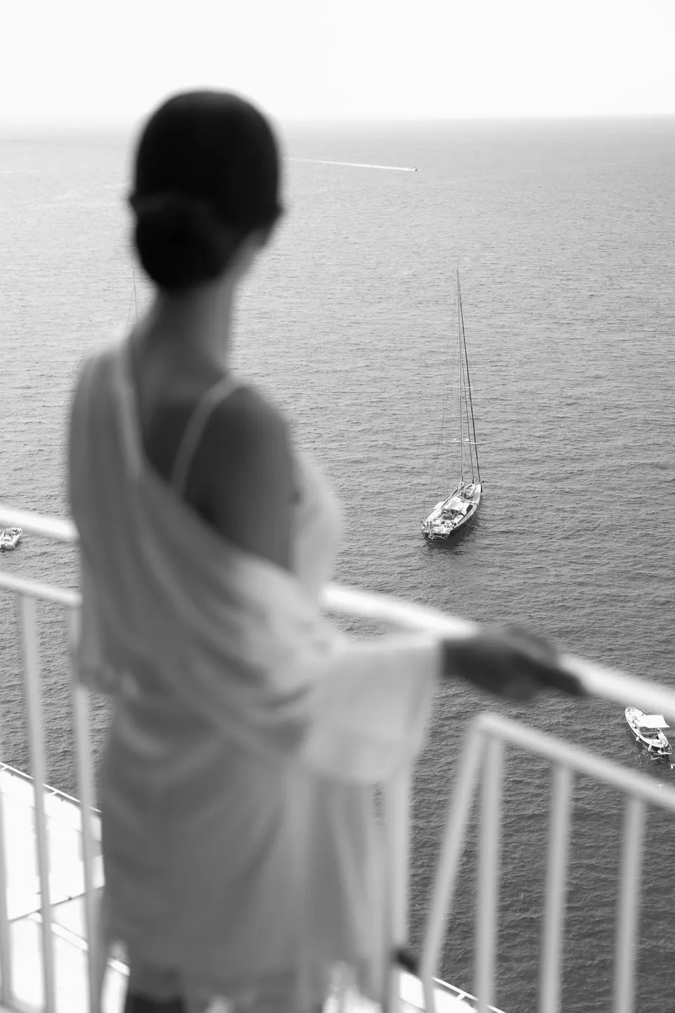 Schwarzweißfoto der Braut im Morgenmantel auf einem Balkon über dem Meer.
