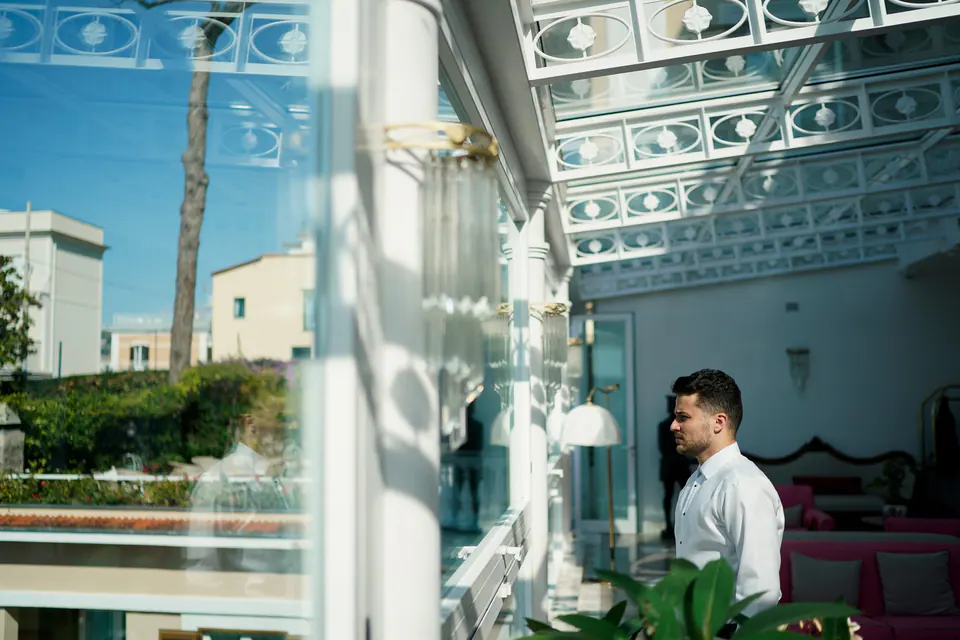 Groom waiting in the glass-roofed room of Hotel Corallo, the sea through the windows.