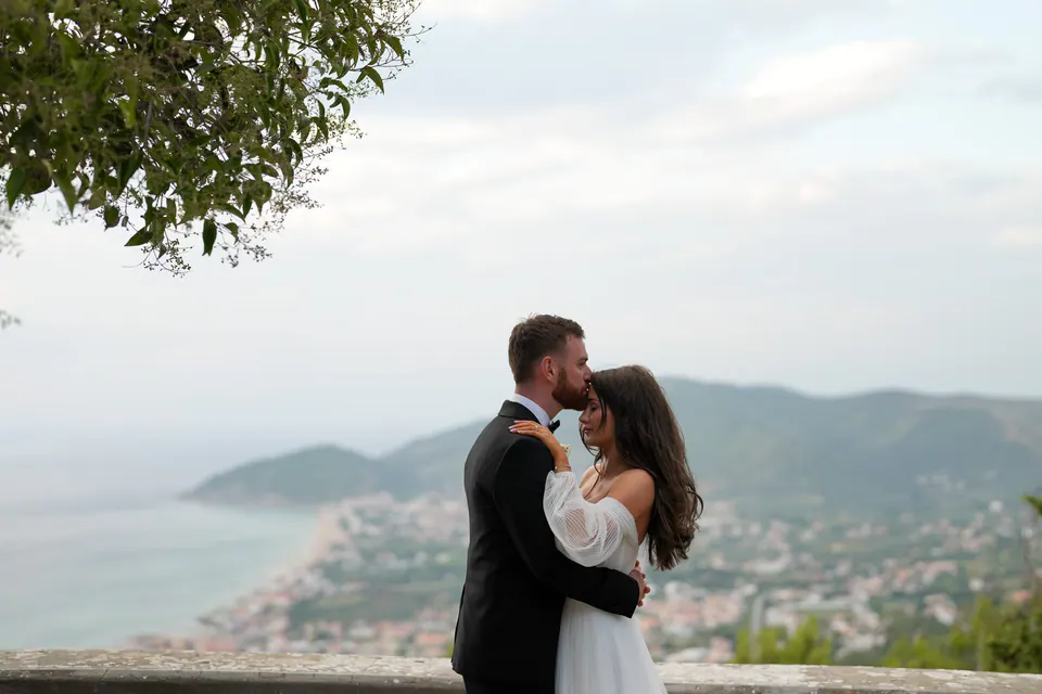 Das Brautpaar umarmt sich auf einer von Bäumen gerahmten Terrasse, unten die Bucht des Cilento.