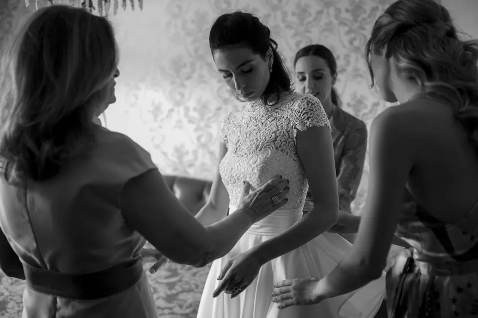 Black and white photo of women fastening the bride's dress