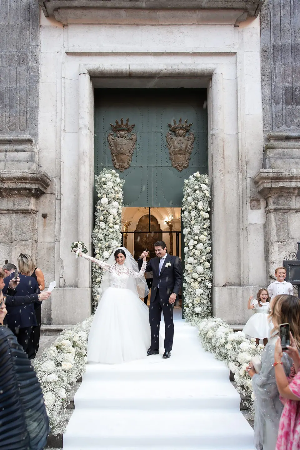 Bride and groom coming out of the church door between white flowers