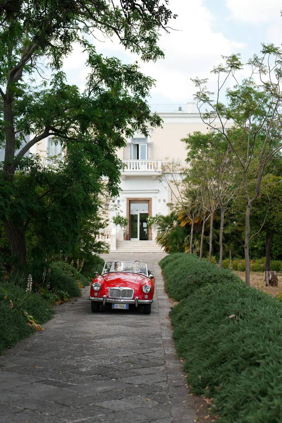 Un deportivo antiguo rojo al final de una avenida del jardín de Tenuta dell’Orso.