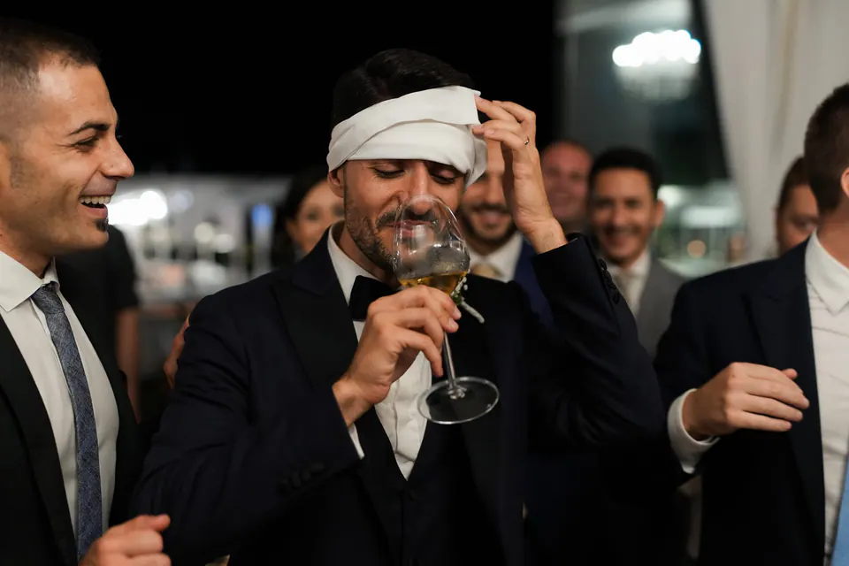 Groom laughing with his friends at the evening party, a playful bandage wrapped around his head.