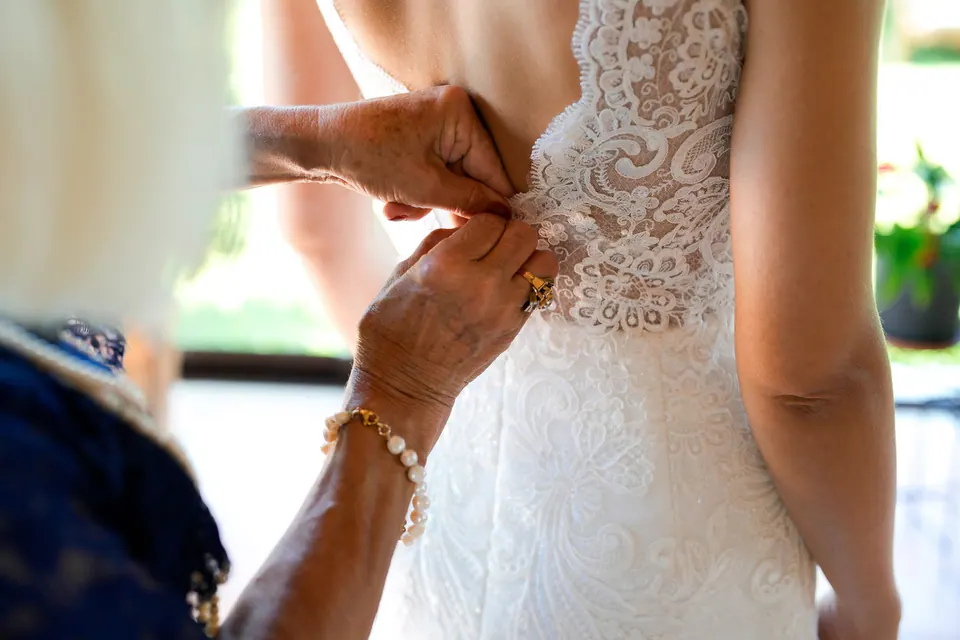 The lace wedding dress being buttoned up at the back by an older woman