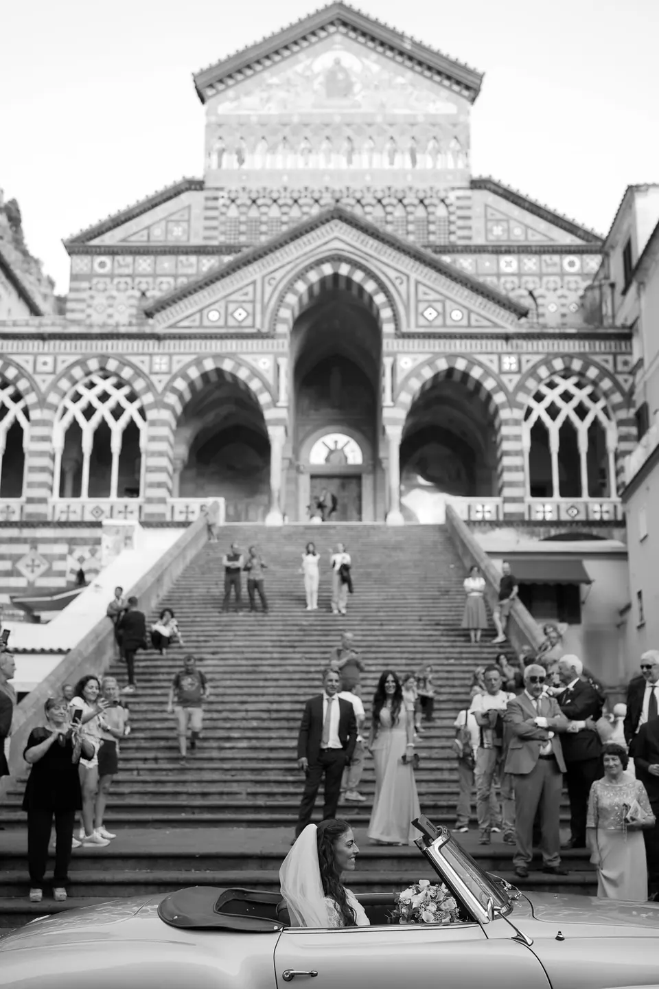 Black and white photo of the cathedral steps in Amalfi, guests and a vintage car below.