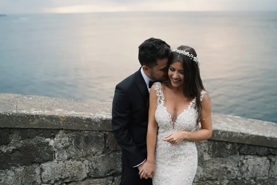 Groom kissing the bride's cheek at the sea wall.