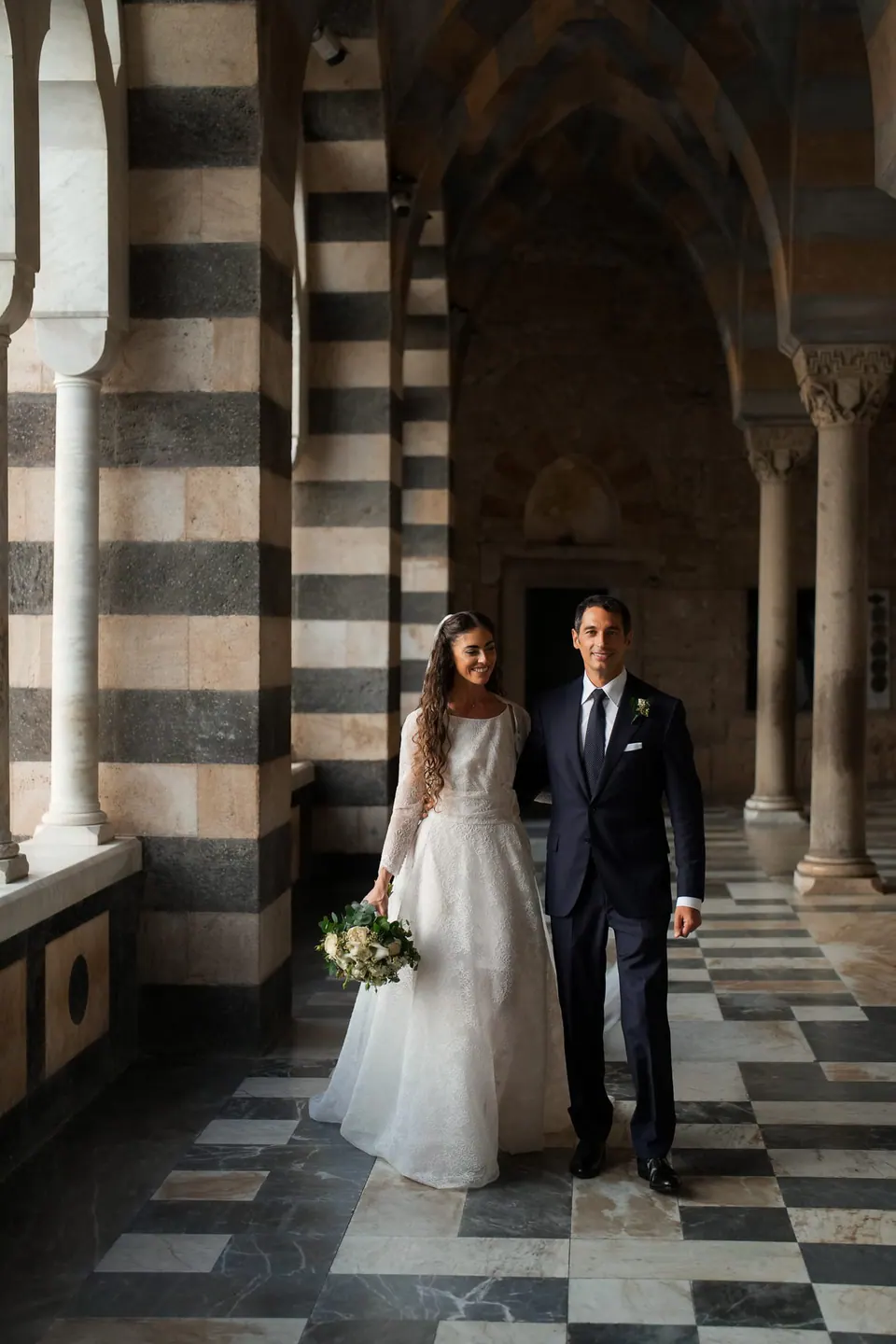 Bride and groom in the atrium of the Amalfi Cathedral, striped arches and a marble floor.