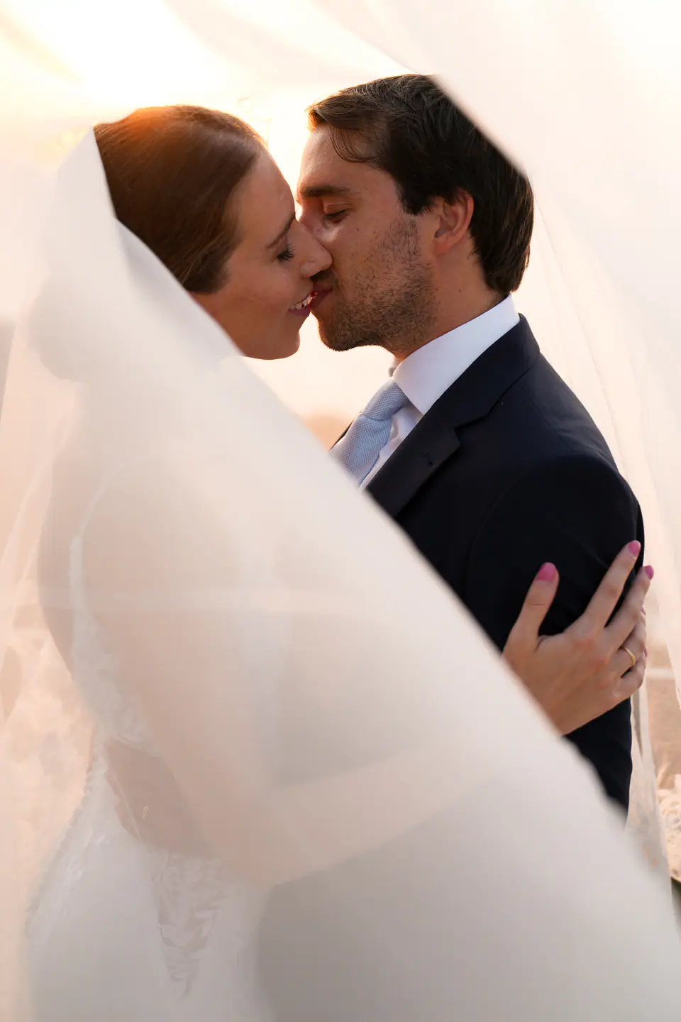Couple kissing under the veil in the warm sunset light.