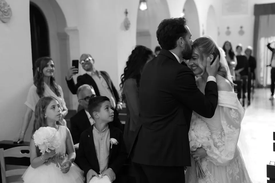 Foto en blanco y negro del novio abrazando a la novia entre los invitados.