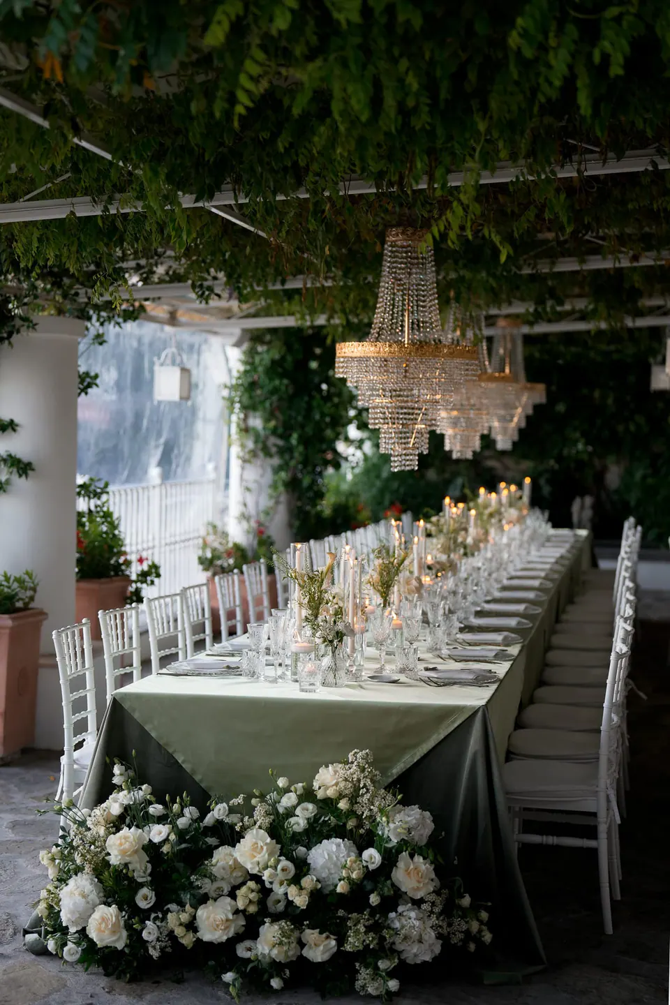 Long table under the pergola with crystal chandeliers and hydrangeas.