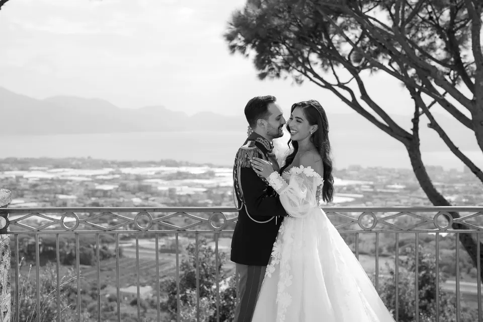 Black and white embrace at the terrace railing, the sea and coast behind them.