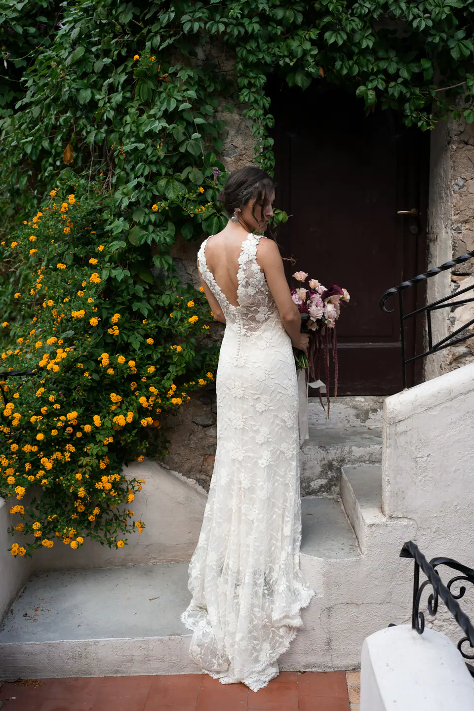Bride in a lace gown on a terrace with orange flowers and a green door.