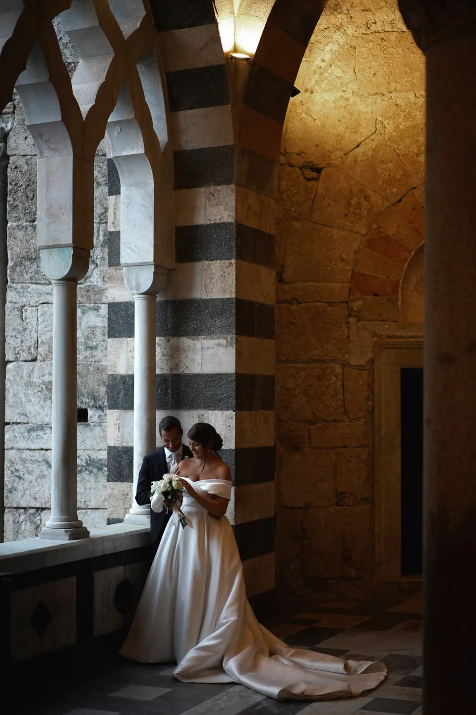 Bride and groom beneath the striped arches of the Amalfi Cathedral atrium.