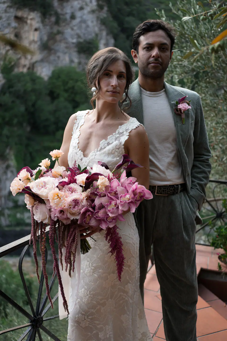 Couple standing on a terrace, her bouquet of pink and burgundy flowers.