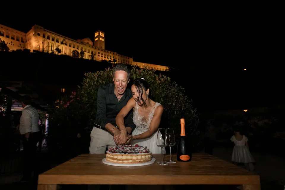 Couple cutting their cake outdoors, surrounded by laughter and candlelight.