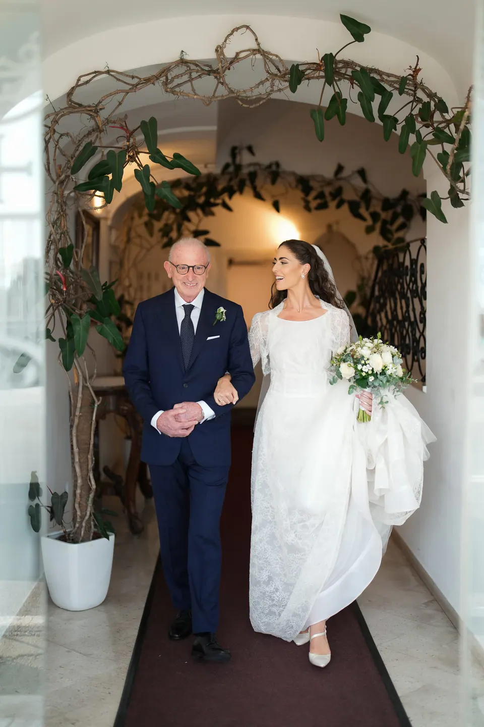 Father walking the bride out through a doorway framed with greenery.