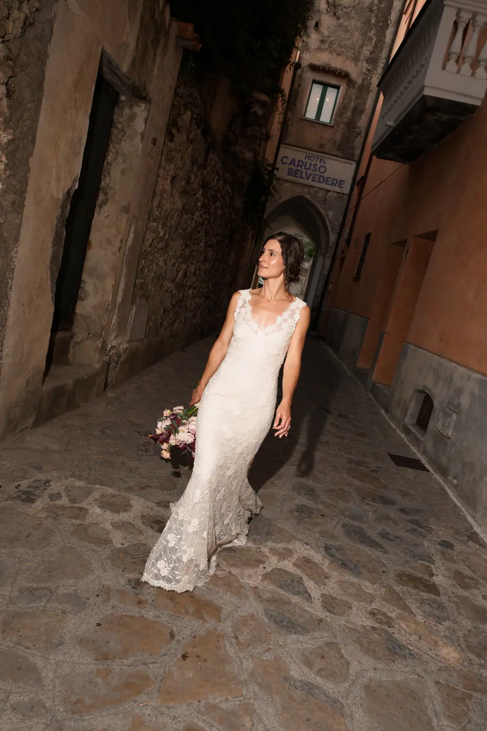 Bride leaning back in a narrow lane of Ravello, laughing.