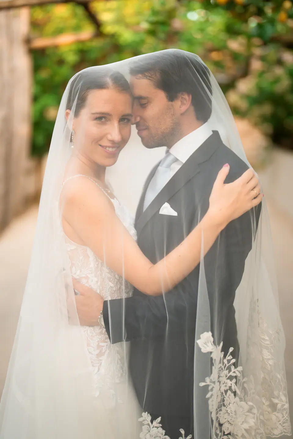 Couple under the bride's veil, smiling under the lemon trees.