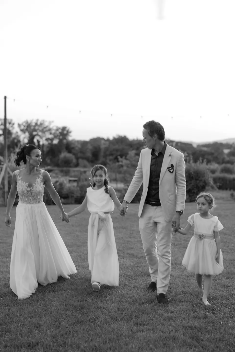 Black and white photo of bride and groom walking with two little girls
