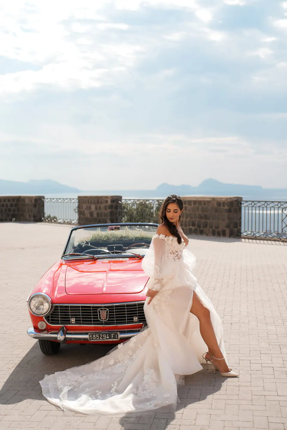 Bride posing by the vintage car with the Bay of Naples in the background.