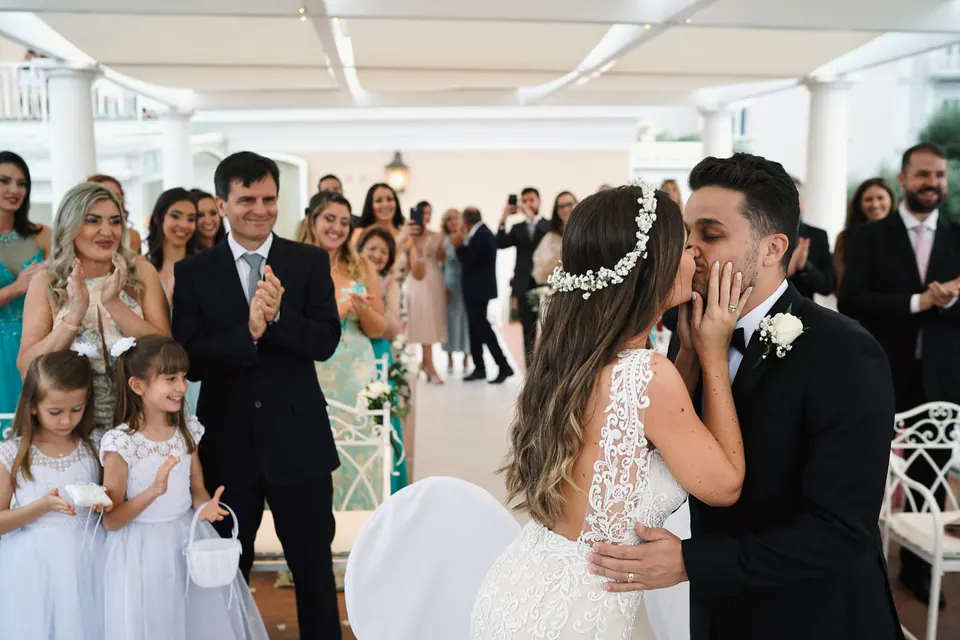 Groom kissing the bride at the altar, flower girls in white beside them.