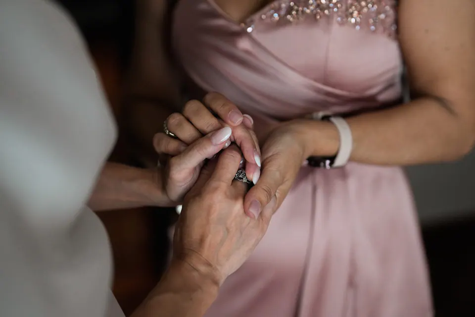 Primo piano delle mani della sposa che stringono quelle di una damigella in rosa.