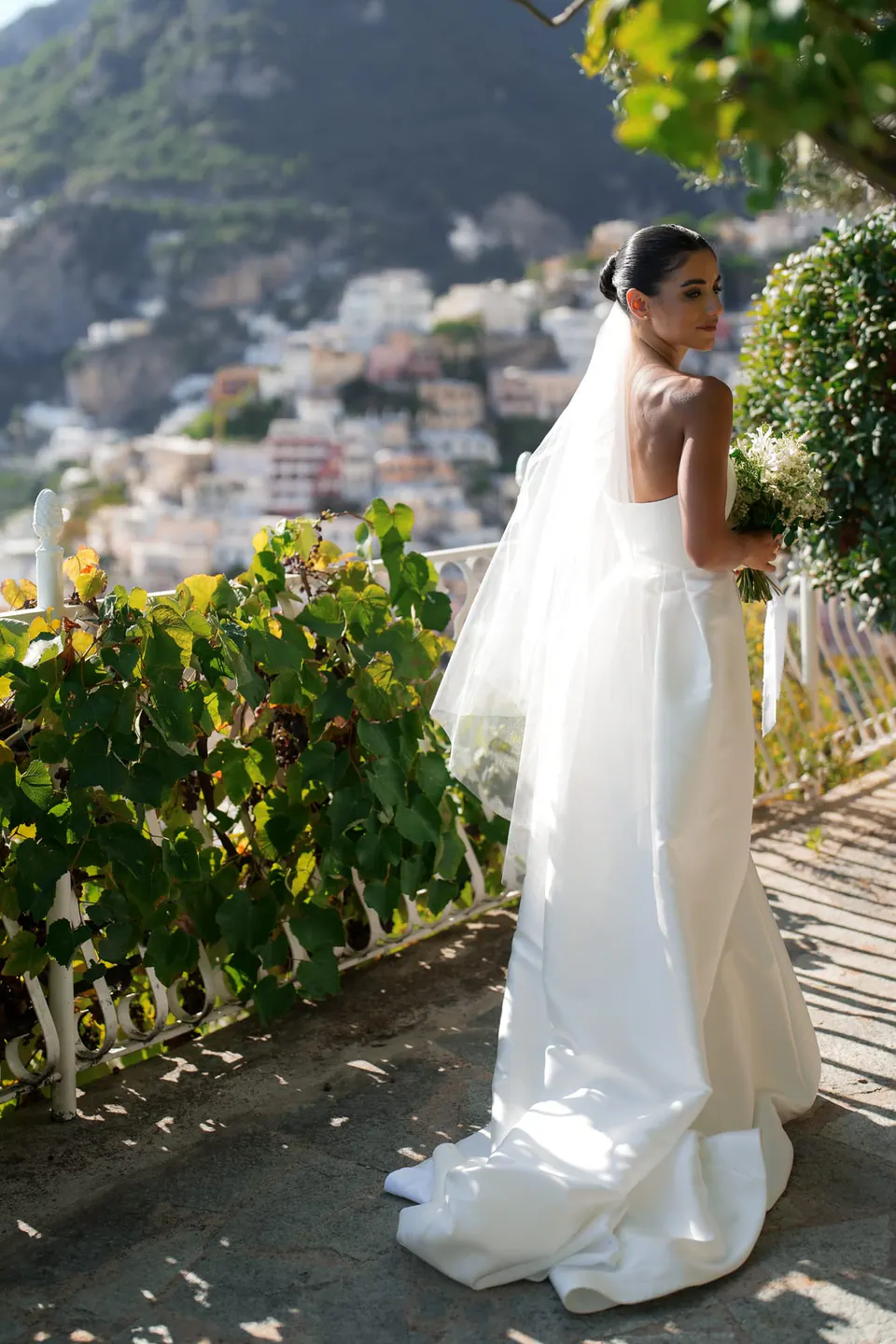 Bride seen from behind on the flowered terrace, her veil trailing.