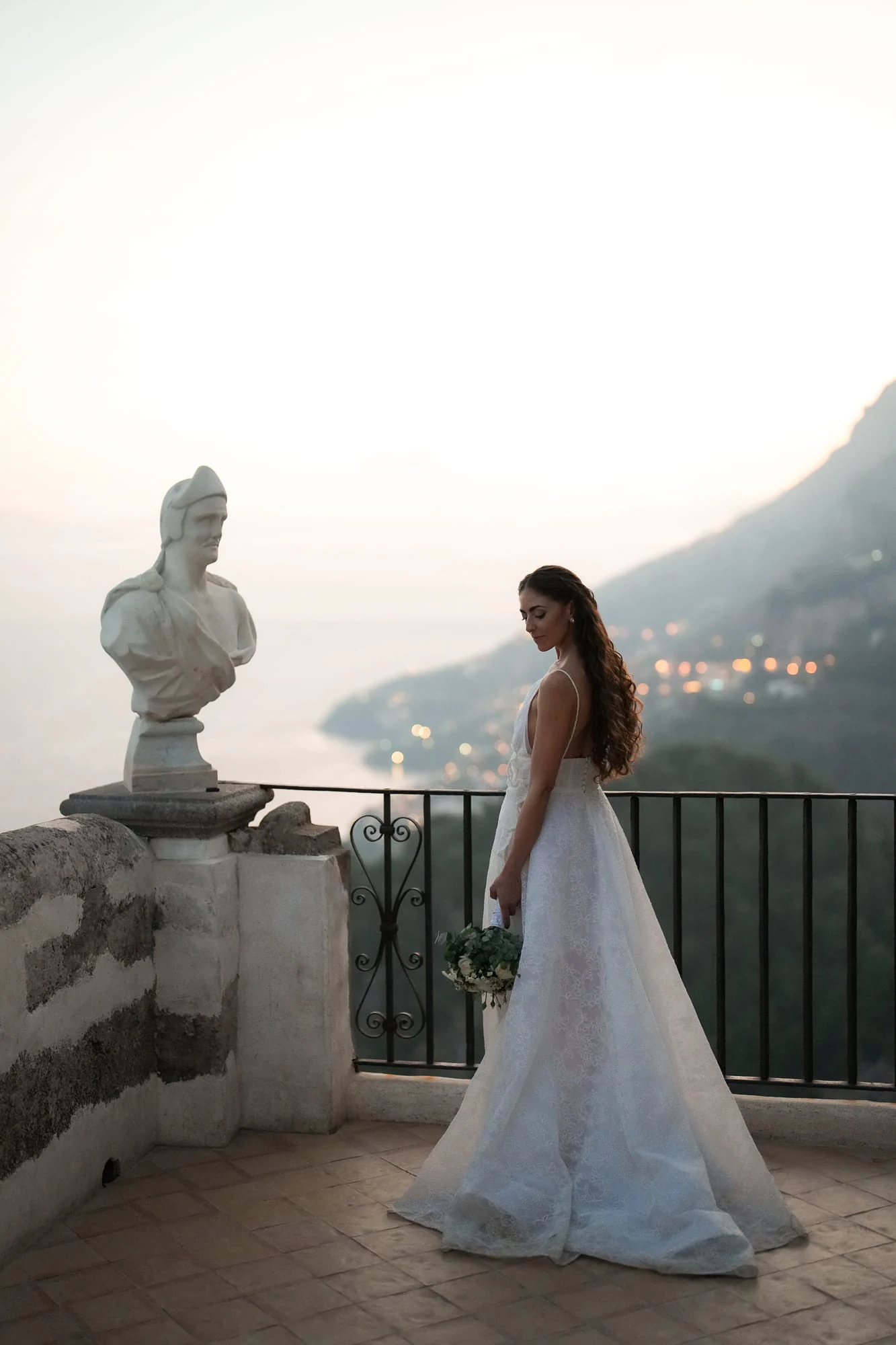 Sposa accanto a un busto in marmo sulla Terrazza dell'Infinito di Villa Cimbrone a Ravello, la Costiera Amalfitana al crepuscolo.