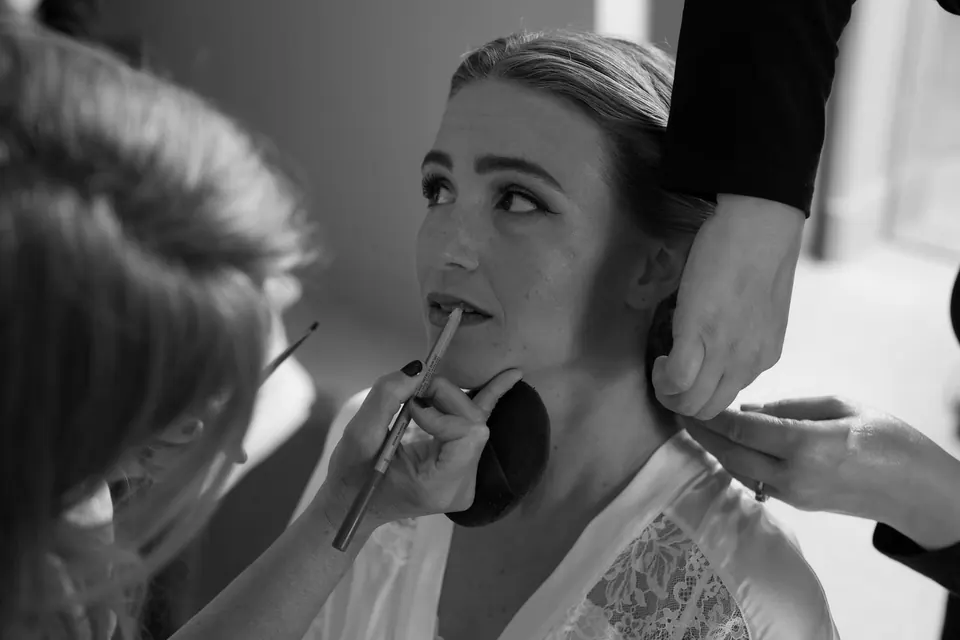 Schwarzweißnahaufnahme: Die Visagistin trägt der Braut Lippenstift auf.