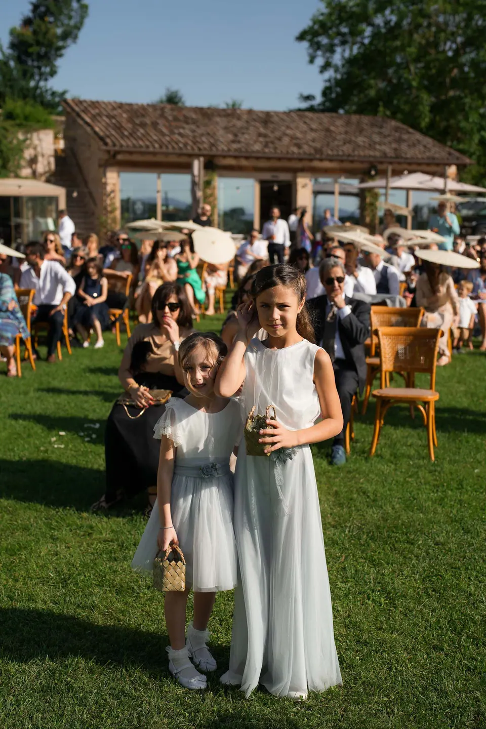 Two flower girls in white on the lawn among the guests