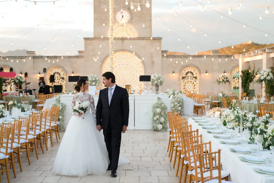 Bride and groom walking between the long candlelit dinner tables outdoors.